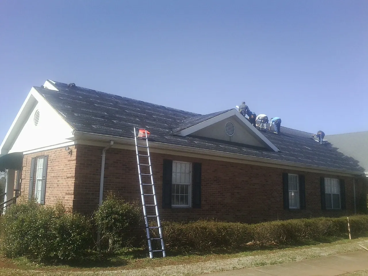Crew tearing shingles off a brick ranch roof with a ladder set — Metal Roof Repair work by our crew in Pinckneyville
