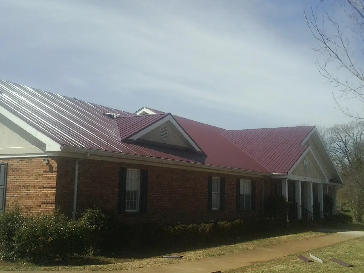 Red metal roof with gabled entries on a long brick building, from a Hail Damage Roof Repair job in Pinckneyville