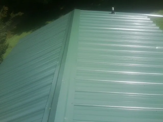New green metal panels meeting at the ridge of a roof — Flat Roof Repair work by our crew in Pinckneyville