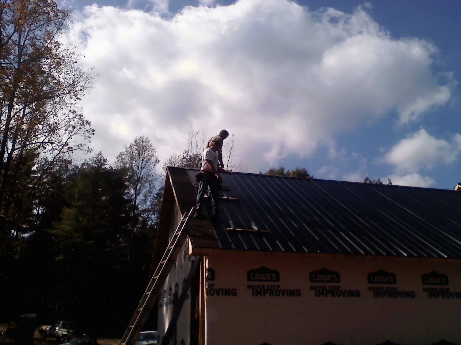 Roofer fastening dark metal panels high against a cloudy sky, from a Roof Inspection job in Pinckneyville