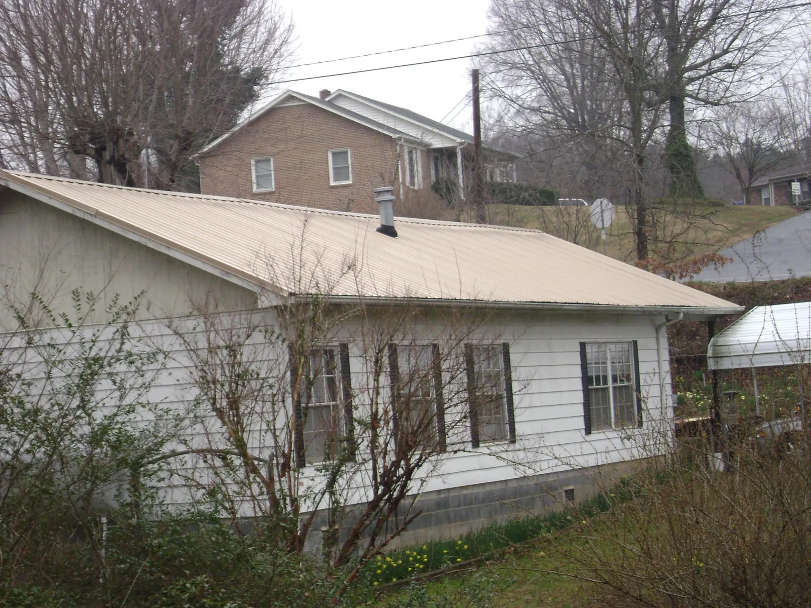 Tan metal roof on a white sided house set into a hillside — Commercial Roofing by Roofing Brothers in Pinckneyville